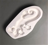 A roughly oval white ceramic mold for fusing hot glass on a grey background. A top-down view of a crawling lizard has been carved into it. The lizard is simple in design and facing downwards. The tip of its tail curls in on itself.