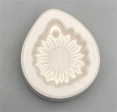 A teardrop-shaped white ceramic mold for fusing hot glass on a grey background. A small, detailed sunflower has been carved into it. There is a post above the top petals allowing for stringing into jewelry after firing.