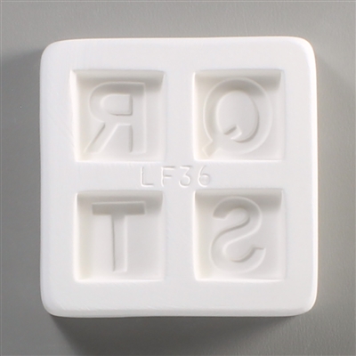 A square white ceramic mold for fusing hot glass on a grey background. Four separate but identically sized squares have been carved into it with equal space between them. Each square has one of the letters Q, R, S, or T carved in block print in it.