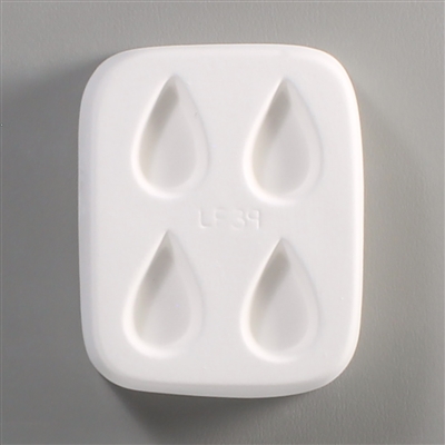 A rectangular white ceramic mold for fusing hot glass on a grey background. Four separate but identical teardrops have been carved into it with equal space between them. LF39 is carved onto the mold between them.