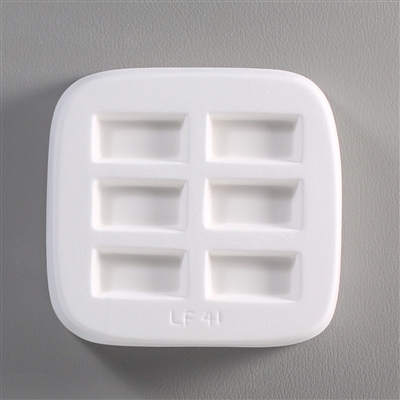 A square white ceramic mold for fusing hot glass on a grey background. Six small separate but identical rectangles have been carved into it with equal space between them. LF41 is carved onto the mold below them.