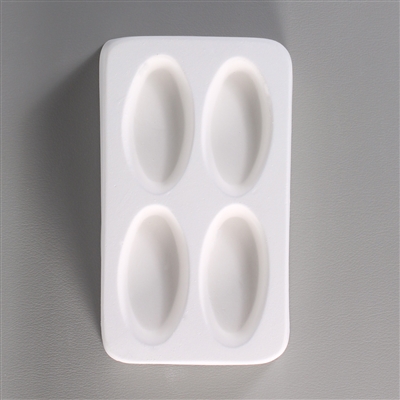 A rectangular white ceramic mold for fusing hot glass on a grey background. Four separate long, thin ovals have been carved into it with equal space between them.