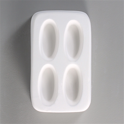 A rectangular white ceramic mold for fusing hot glass on a grey background. Four separate long, thin ovals have been carved into it with equal space between them.