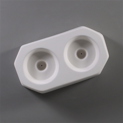 A white ceramic mold for fusing hot glass on a grey background. Two separate identical circles have been carved into it with a space between them. Each circle has a deeper circle in the center with a small vent hole in the very center.