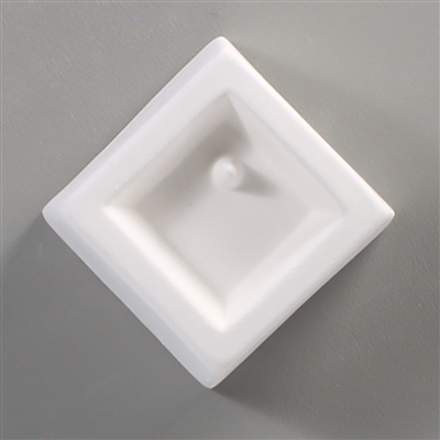 A square white ceramic mold for fusing hot glass on a grey background. A square has been carved into it. There is a post towards the top corner of the square allowing for the resulting glass to be strung as jewelry.