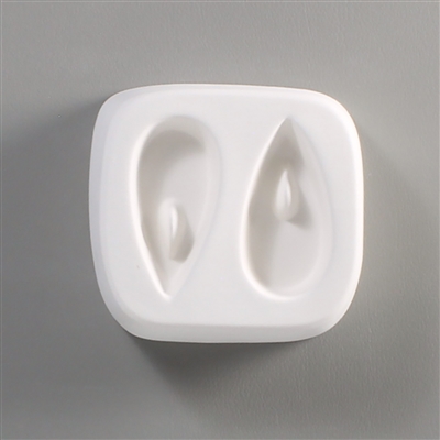 A square white ceramic mold for fusing hot glass on a grey background. Two identical long teardrops have been carved into it. There is a post towards the top of each tear allowing for the resulting glass to be strung as jewelry.