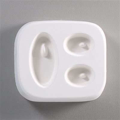 A white ceramic mold for fusing hot glass on a grey background. Three ovals have been carved into it, one large on the left and two smaller to the right. There is a post towards the top of each oval allowing for the resulting piece to be strung as jewelry