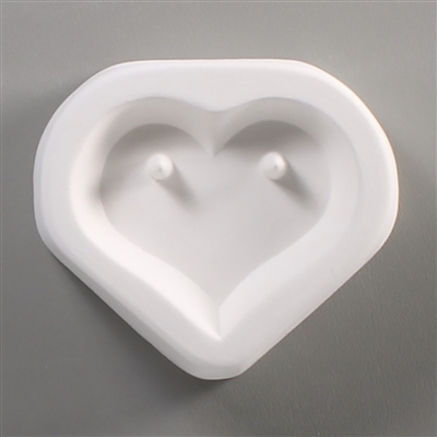 A triangular white ceramic mold for fusing hot glass on a grey background. A heart shape has been carved into it. There is a post on either side of the top of the heart allowing for the resulting glass piece to be strung or otherwise hung.