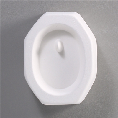 An octagonal white ceramic mold for fusing hot glass on a grey background. An oval has been carved into it. There is a post towards the top of the oval allowing for the resulting glass piece to be strung as jewelry.