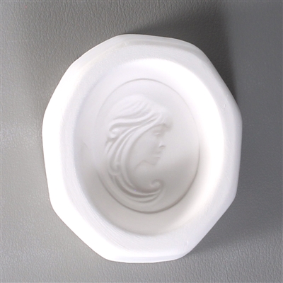 An octagonal white ceramic mold for fusing hot glass on a grey background. An oval-shaped cameo style design of a womanâ€™s face looking right with her hair sweeping around her has been carved into it.