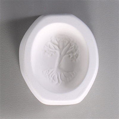 An octagonal white ceramic mold for fusing hot glass on a grey background. An oval-shaped cameo style design of a tree with sprawling branches and roots has been carved into it.