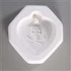 An octagonal white ceramic mold for fusing hot glass on a grey background. An inverted tear-shaped cameo style design of a skull and crossbones has been carved into it. There is a post above the skull allowing for the final piece to be strung.