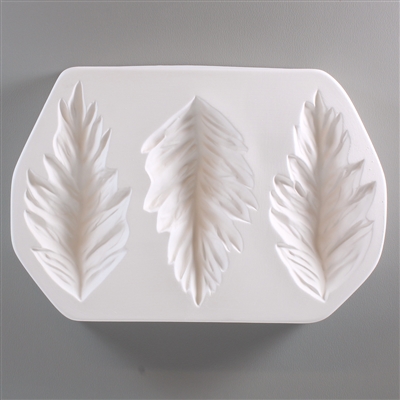 A roughly rectangular white ceramic mold for fusing hot glass on a grey background. Three large separate detailed leaves have been carved into it. Each leaf is carved quite deep. The middle leaf is slightly wider and shorter than the two on the sides.