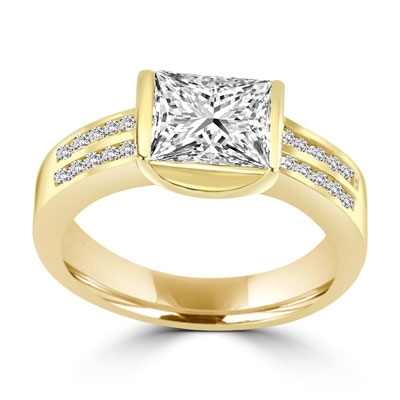 A unique East-West design, with a Channel Set 1.5 Ct. Radiant Emerald Cut Diamond Essence Centerand a bevy of Melee accents down the band for an exhilarting sensation in 14K Solid Gold.