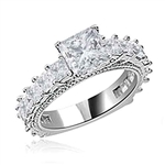 Diamond Essence Designer Ring With 1.50 Cts. of Princess in Center, Accompanied by Small Princess Stones Melee on band, 3 Cts.T.W. In Platinum Plated Sterling Silver.