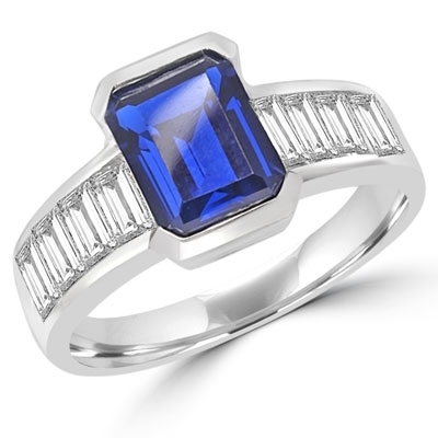 Escape with this Wide Band Ring with Channel Set Emerald Cut Sapphire Essence, 2.5 cts. separated by straight Diamond Bright Baguettes set vertically for a totally magnificent effect. 3.5 cts. T.W. set in 14K Solid White Gold.