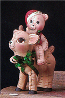 A small ceramic deer with a small ceramic bear on its back. Both have been styled to look like stuffed toys. The deer is standing and looking up, and the bear has a red hat and vest. Both are slightly different shades of brown. The deer has a green ribbon