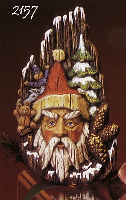 A scene of cast ceramic depicting Santa's face. He is surrounded by a couple toys, a few pinecones, and a green fir tree. The entire piece is textured to look like it was painted on wood.