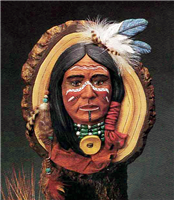 A cast ceramic piece depicting the face of a Native American man. He looks forward  and wears several beaded necklaces. His face is painted with white and red designs. The face is displayed on another cast ceramic piece made to look like a slice of wood.