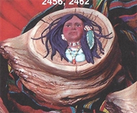 A box made of cast ceramic styled to look like a rough-hewn piece of wood. It has a cast ceramic lid that looks like a log slice with a design of a Native American woman looking forward on top. Her  hair is blowing in the wind and has a feather in it.
