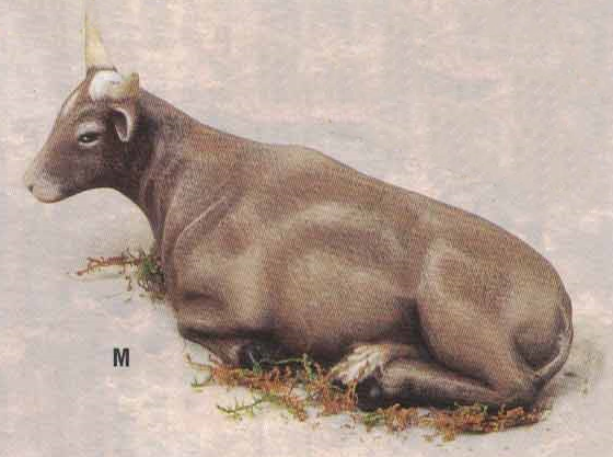A small cast ceramic figure of a cow laying down. It is medium brown with light brown highlights, and a white diamond on its forehead. Its two small horns are white, and its hooves are black. Its tail is wrapped between its back legs.