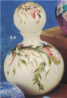 A round vase-like decanter made of two pieces of cast ceramic. The body is spherical with a thin round neck, and the lid is a large sphere with a stopper. Both are glazed white and painted with a delicate green and pink floral design.