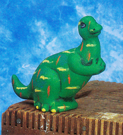 A cast ceramic figure of a simplified bipedal dinosaur. Its neck is slightly elongated and its snout is rounded. Its arms are held in front of its body, and it looks up. It is painted green with yellow and orange zigzag lines scattered across its body.