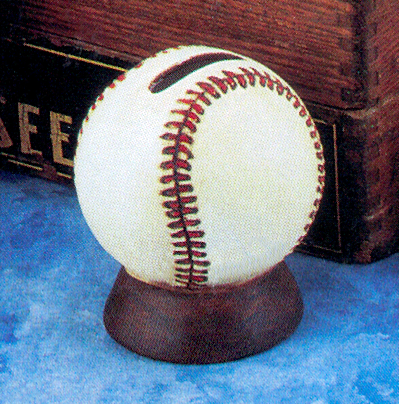 A cast ceramic figure of a baseball on a small brown stand. There is a small rectangular slit is cut in the baseballâ€™s top to turn the piece into a piggy bank. The stand is cylindrical and tapered towards the top where the baseball sits.