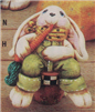 A ceramic figure of a long-eared rabbit in overalls. It is sitting on a barrel and eating a large carrot, which it holds in its right hand. Its overalls are lime green and it wears a yellow scarf with black stars. Its fur is white.