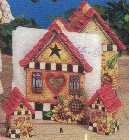 A cast ceramic napkin holder shaped like a house, flanked by two smaller cast ceramic salt and pepper shakers shaped similarly. The houses are decorated the same- red roof, yellow walls, black and white checkerboard trim. Each has a couple sunflowers.