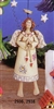 A cast ceramic figure of a stylized, smiling angel. She is hung from a branch and her legs are attached in such a way that they dangle from her body and move as she moves. She wears a long white dress and has small wings and a halo above her head.