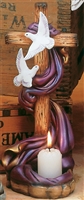 A cast ceramic scene. The main piece is a large wooden cross with a flowing purple scarf wrapped around it. The scarf flows into a stone-textured base with a place to hold a votive candle. There are two flying doves attached to the body of the cross.