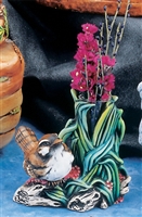 A cast ceramic figure of a small bird resting on a log next to winding leaves. The leaves wind upward and create a small thin vase for holding flowers. The bird is painted brown, black, and white to resemble a sparrow.