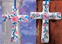 Two flat cross ornaments made of cast ceramic. The right is slightly longer. The base of each is painted white, and both have floral designs with pink flowers and winding green leaves painted on top. They are hung up with thin blue ribbons.