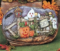An oval-shaped cast ceramic stone slab placed in a cast ceramic rock base. The slab shows a picket fence with Beware of Ghost! sign. Two ghosts peer out from behind the fence. One end is falling apart, and there are two carved pumpkins in front.