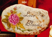 A cast ceramic stone slab that is oval in shape and flat on either side. It features a detailed flower similar to a peony surrounded by green leaves, vines, and buds on the left and the words Love Blooms carved in curved font on the right.