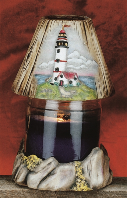 A candle placed inside a cast ceramic holder with a cast ceramic shade on top. The holder is shaped like a ring of stones with moss. The shade is textured like wooden planks and has the design of a lighthouse on a hill embossed on the front.