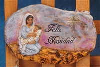 A cast ceramic stone slab that is oval in shape and flat on either side. It shows a kneeling Mary holding a swaddled baby Jesus on the left. The words Feliz Navidad are carved in elegant print to their right. A large star is carved in the sky to the right