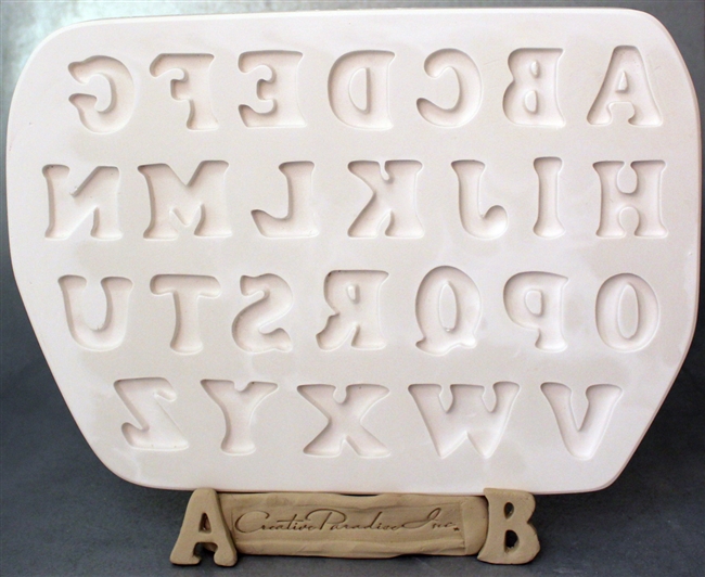 A white plaster mold for pressing moist clay into specific shapes. The 26 letters of the English alphabet are carved into it in four rows. They are in a tall, block font.