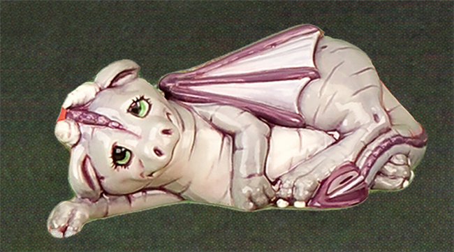 A small cast ceramic figure of a dragon laying on its side. One arm is out supporting its head while the other is draped across its body. Its legs and tail are curled up and its wings are wrapped around it. Its half-closed eyes look upwards.