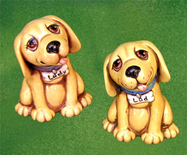 Two small cast ceramic dogs. They are identical. Both are seated, looking slightly upward with heads cocked to the left. They have floppy ears and their tongues are out. They wear collars with bone shaped tags and have wide eyes.