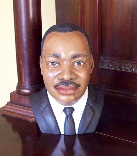 A cast ceramic bust of historic American activist Martin Luther King Jr. He looks forward confidently, wearing a suit jacket, collard shirt, and simple tie.