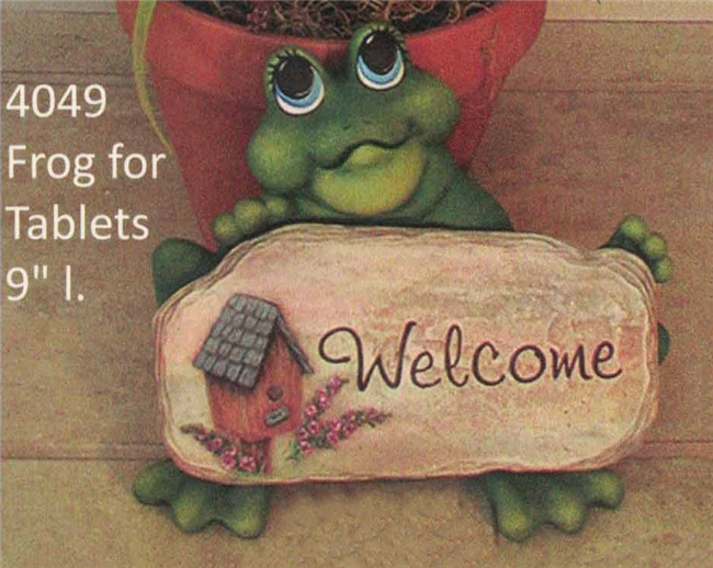 A seated cast ceramic frog looking upward and holding vaguely rectangular cast ceramic tablet. The tablet has a birdhouse surrounded by three conical strings of flowers embossed on the right and the word Welcome carved in a curving print on the left.