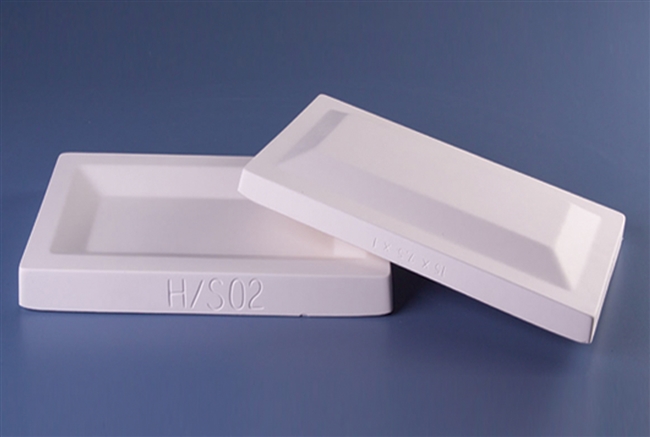 A set of two white plaster molds for pressing moist clay into shapes. Both are rectangular in shape. One mold has a rectangular depression carved into it with angled sides. The other mold has the same shape, only inverted and raised instead of carved.