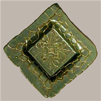 A square dish made of ceramic. It has a square depression in the center. The rim is textured to look like assembled mosaic pieces and there is a somewhat floral embellishment texture in the center.