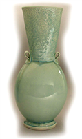 An oval bodied vase with an inverted conical neck. It has two small loops as handles where the neck meets the body, and a flat circular base. The neck is textured with a floral pattern and the body is smooth. It is glazed with a pale green.