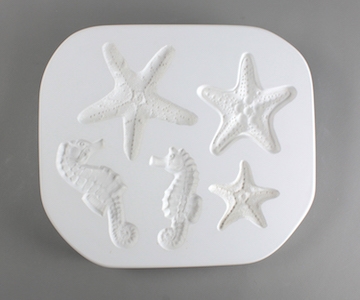 A white plaster mold for pressing moist clay into specific shapes. Three starfish and two seahorses are carved into it. The starfish are different sizes and all have a slightly different pattern. The seahorses are two sizes and face opposite directions.