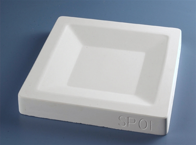 A white plaster mold for pressing moist clay into shapes on a blue background. It is square in shape, with a smaller square carved into the center surrounded by angled edges.