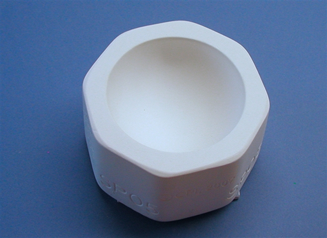 A white plaster mold for pressing moist clay into shapes on a blue background. It is octagonal in shape. An inverted circular dome is carved into the center.