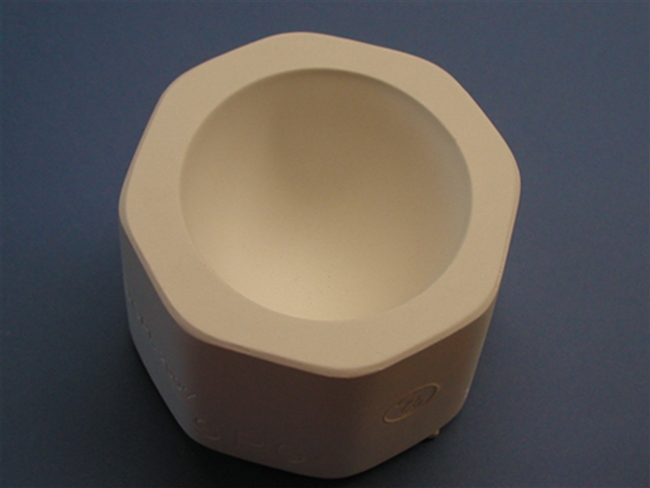 An off-white plaster mold for pressing moist clay into shapes on a blue background. It is octagonal in shape. An inverted circular dome is carved into the center. The top tapers as it goes down, similar to the top of an egg.